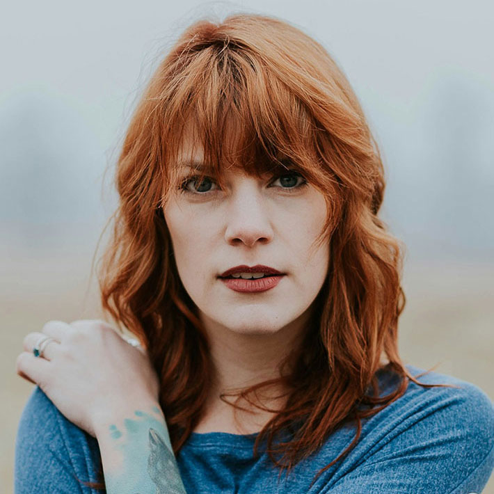 Portrait of Sophia Carter, BrainStak's crypto analyst, with red hair and blue shirt, looking confidently at the camera.