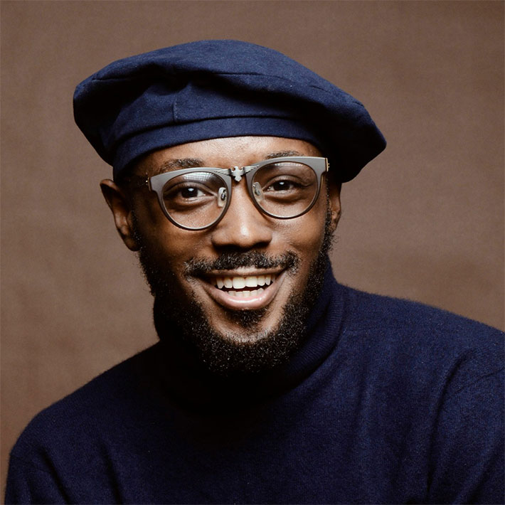 Portrait of Liam Bennett, wearing a blue cap and glasses, smiling in front of a grey background.